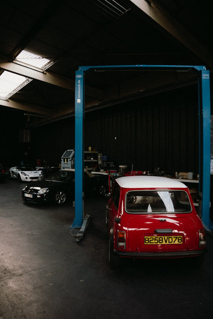 A vintage Red Mini Cooper parked in a dimly lit garage with other classic cars.
